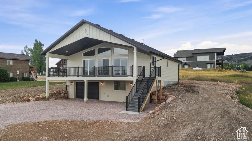Board and batten siding, vaulted covered deck with black railing, large sliding glass doors, lower-level garage access, and exterior staircase with black railing