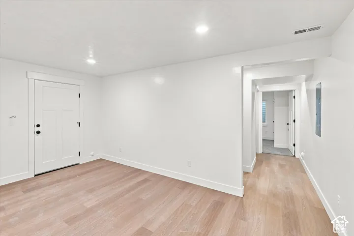 Light-toned wood-finish flooring, recessed lighting, white trim, white paneled door with black hardware, and a white wall finish