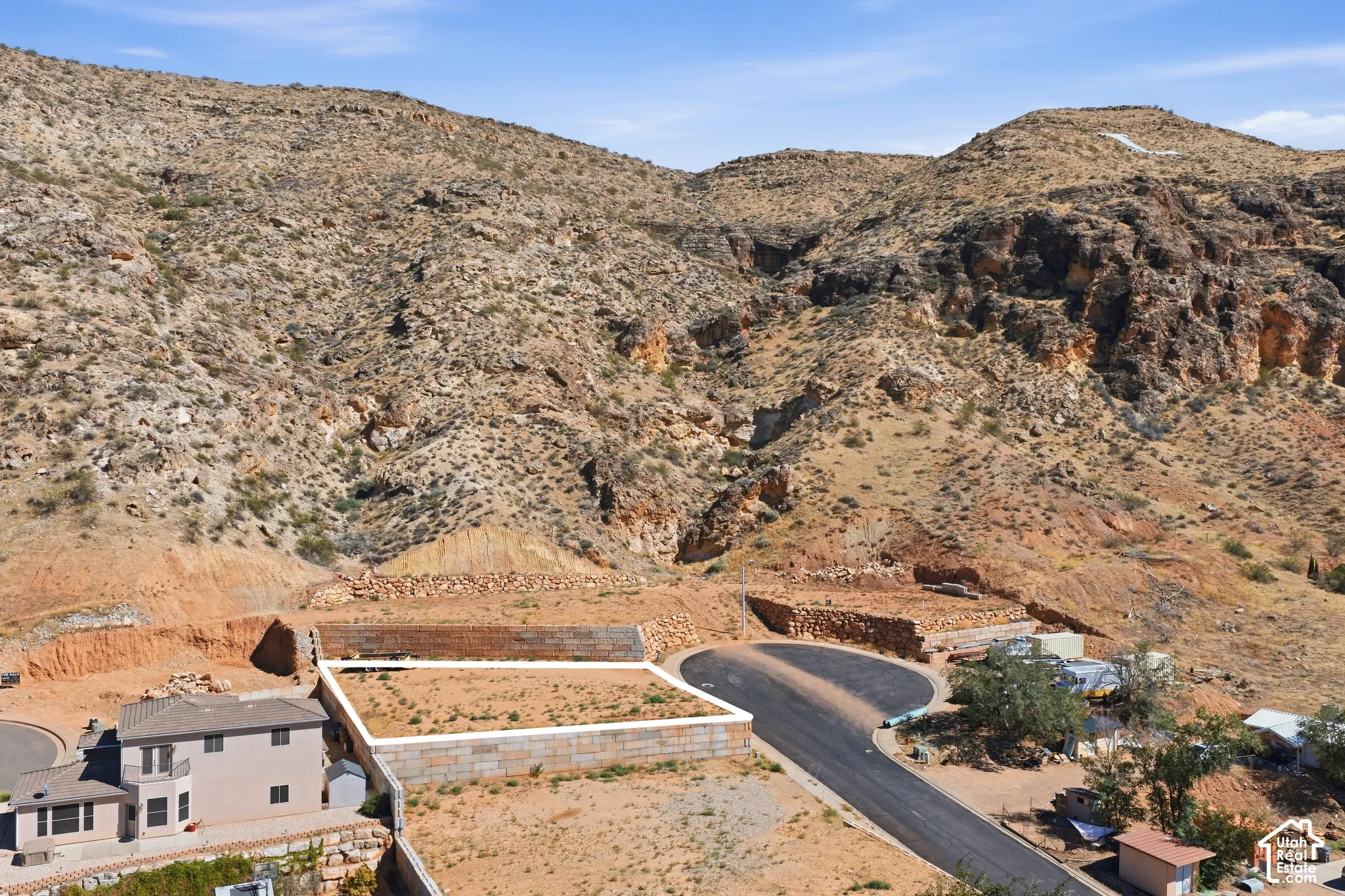 Terraced building lot with retaining walls, paved road access, and desert mountain backdrop