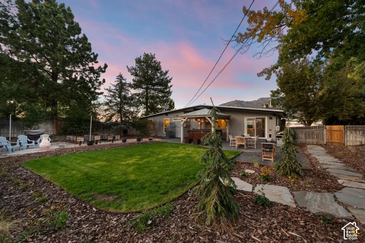 Expansive backyard featuring a manicured lawn, a stone patio, and a covered outdoor living area