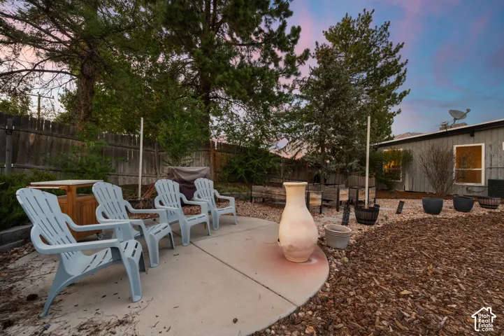 Outdoor concrete patio area featuring a privacy fence, mature trees, and a wood chip ground cover