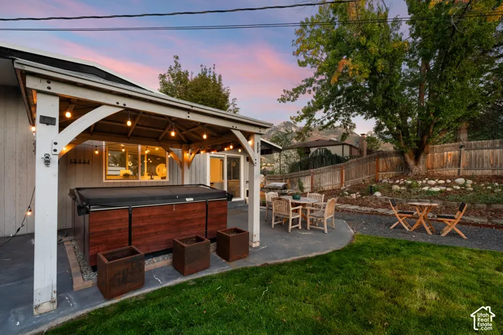 Patio with an integrated hot tub, covered pergola, and string lighting