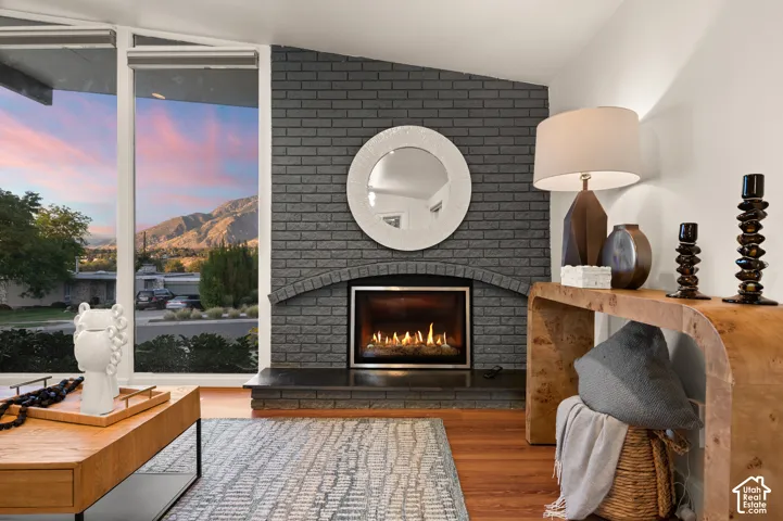 Floor-to-ceiling windows, brick fireplace with arched detail, wood-finish flooring, and crisp white walls