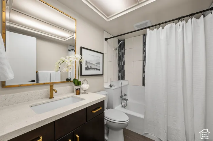 Recessed lighting, gold-tone framed mirror, dark wood-finish vanity with gold-tone hardware, light speckled countertop, and a tiled shower surround with a built-in tub