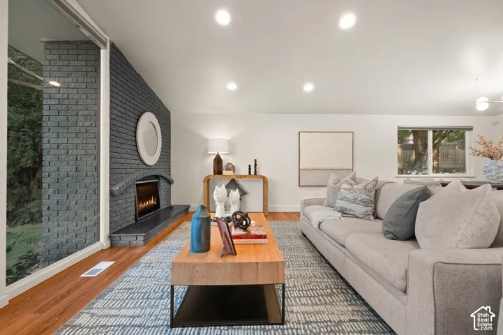 Living area featuring a brick fireplace with a stone hearth, recessed lighting, and wood-finish flooring