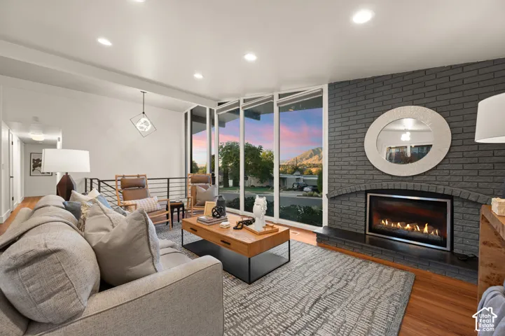 Recessed lighting, wood-finish flooring, full-height windows, a gray brick fireplace with an integrated firebox, and a metal railing