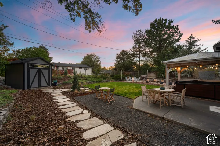 Expansive backyard featuring a stone pathway, a substantial storage shed, a covered patio structure, and a hot tub
