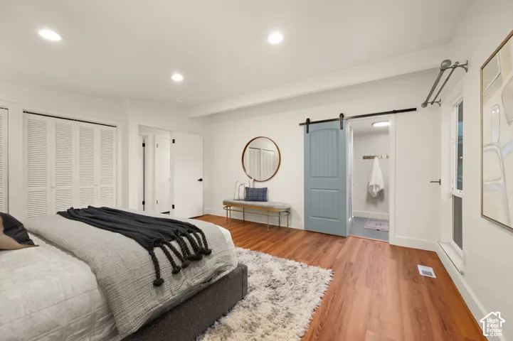 Wood-finish flooring, recessed lighting, white louvered closet doors, modern barn door, and a white window frame