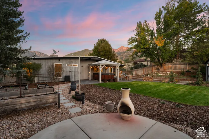 Expansive backyard featuring a manicured lawn, established trees, and a covered patio with a built-in hot tub