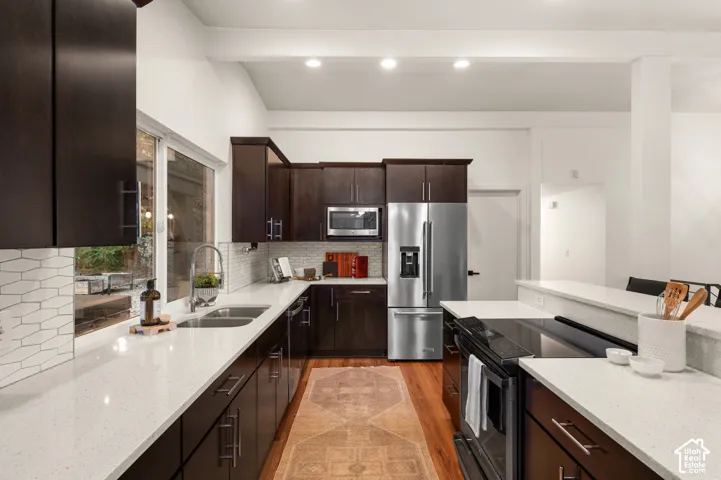Kitchen featuring dark wood cabinetry, light-toned countertops, stainless steel appliances, and a tile backsplash