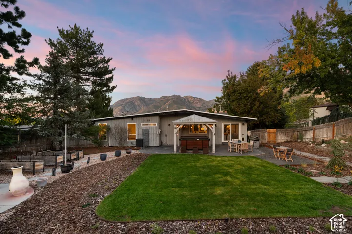 Expansive backyard featuring a manicured lawn, a paved patio with a pergola, raised garden beds, and mountain scenery