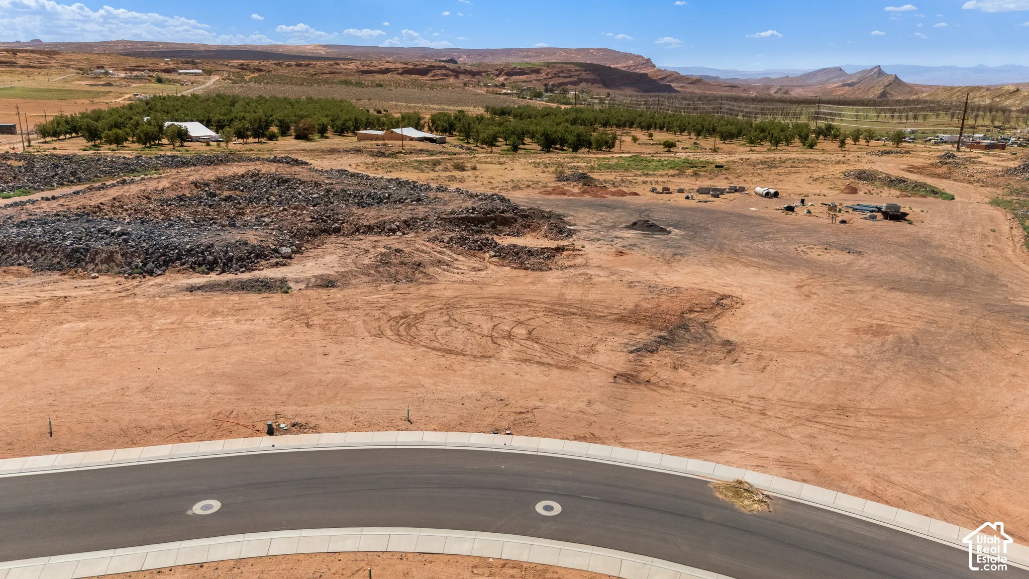 Expansive cleared lot with paved road frontage, surrounded by distant mountains and scattered green foliage