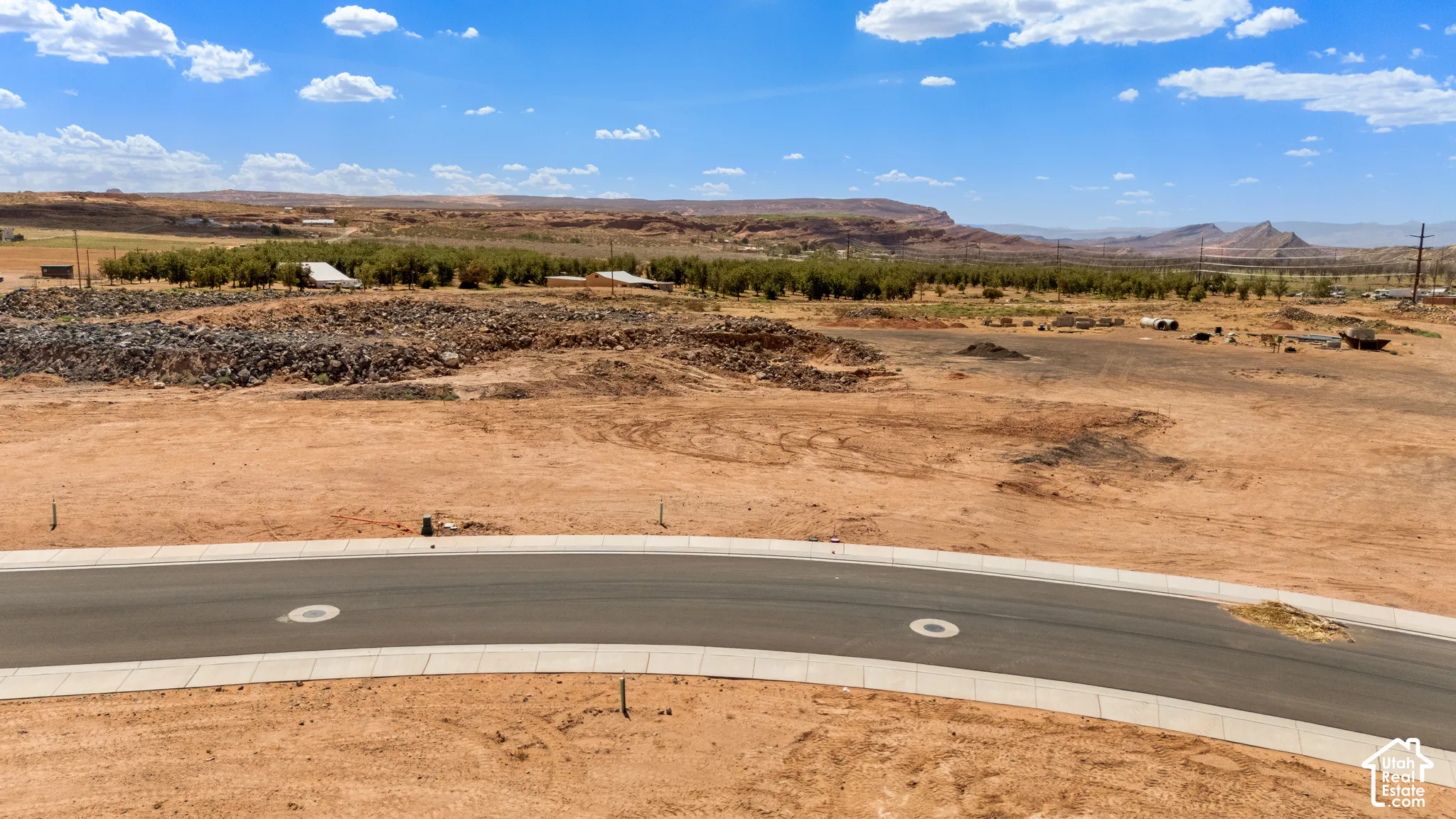 Paved street frontage with integrated curbs, undeveloped land, and distant natural rock formations
