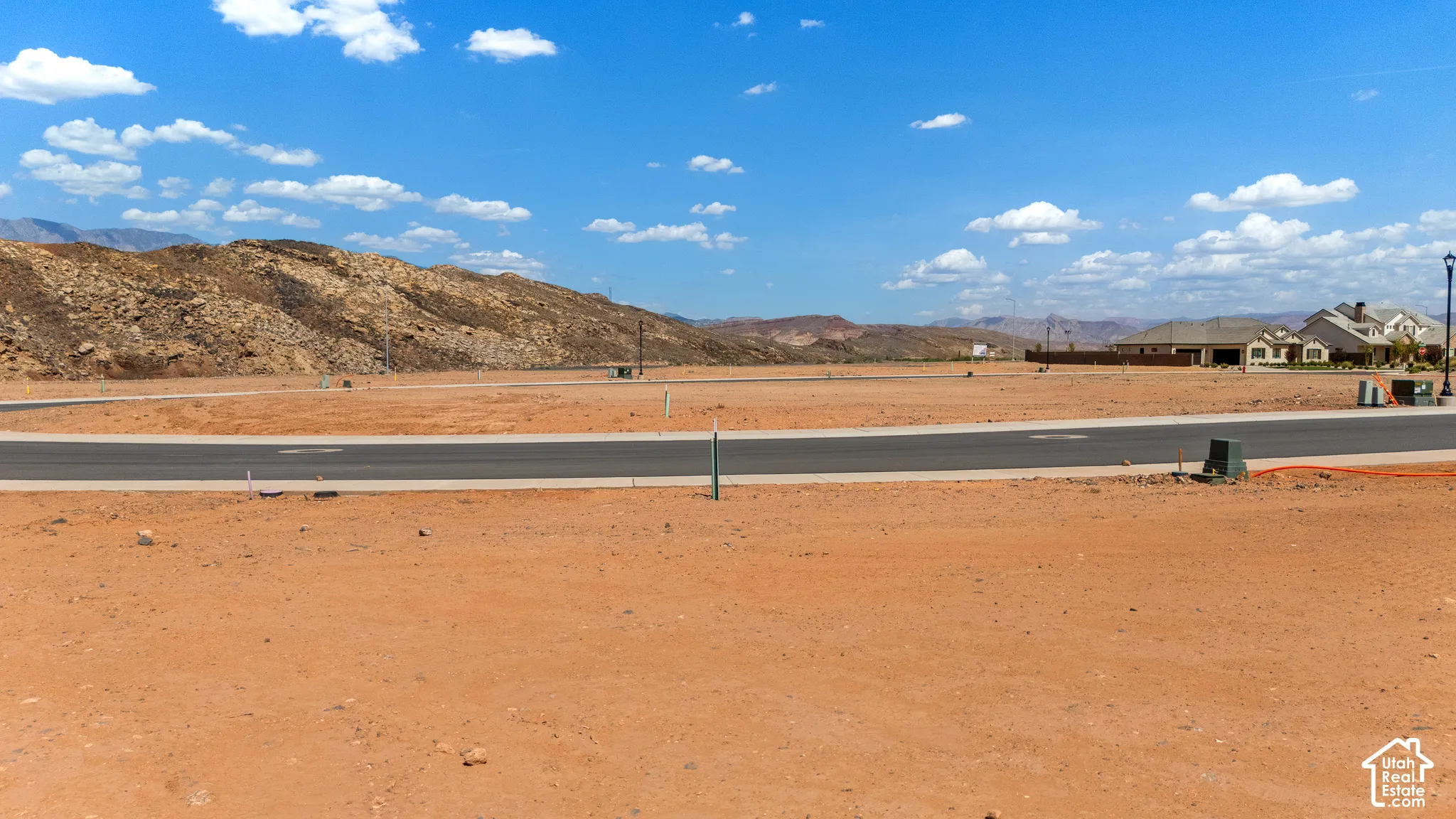 Expansive undeveloped lot featuring a paved road, utility infrastructure, and distant mountain backdrop