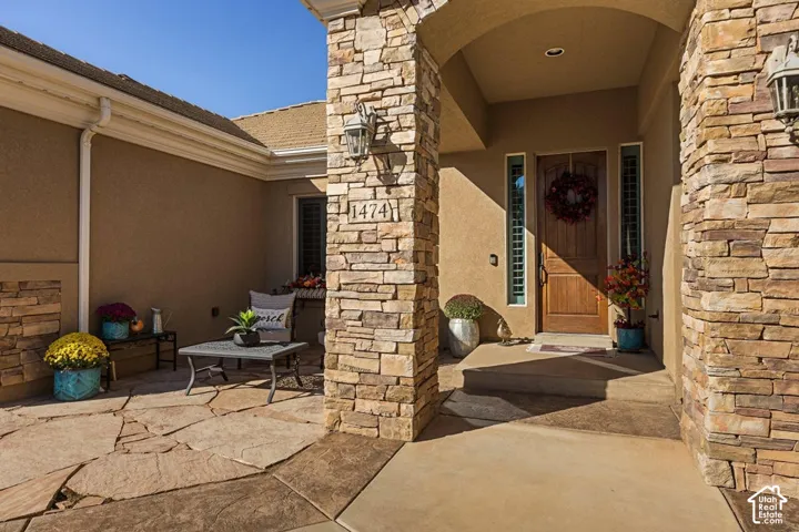 Stone veneer exterior columns, wood-paneled entry door, vertical transom windows, exterior sconce lighting, and flagstone patio