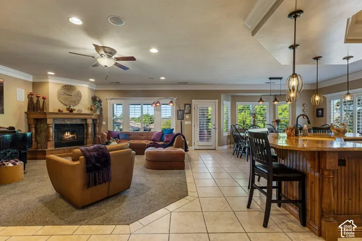 Recessed lighting, ceiling fan, fireplace with stone surround, kitchen island with built-in seating, and tile flooring