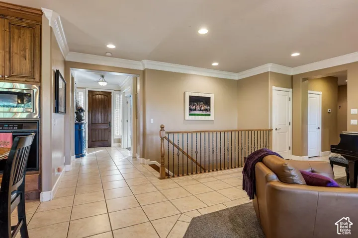 Warm neutral wall tones, crown molding, recessed lighting, tile flooring, and a dark wood entry door with sidelights