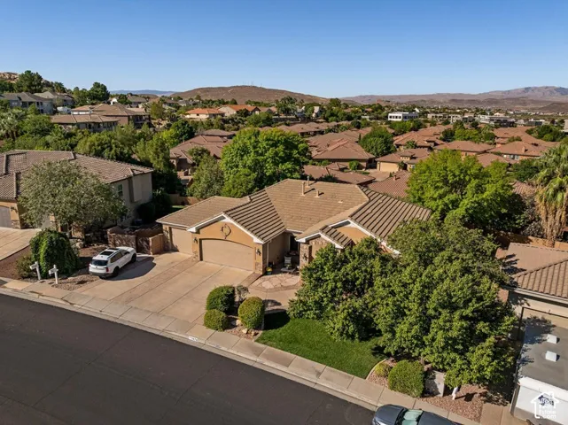 Exterior featuring a tile roof, stucco finish, attached garage, paved driveway, and mature landscaping