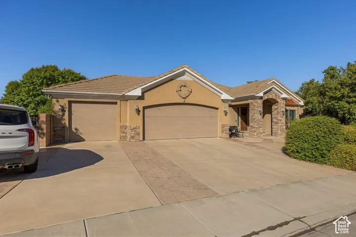 Stucco exterior with stone accents, two garage doors, concrete driveway with decorative inlay, and a covered entry