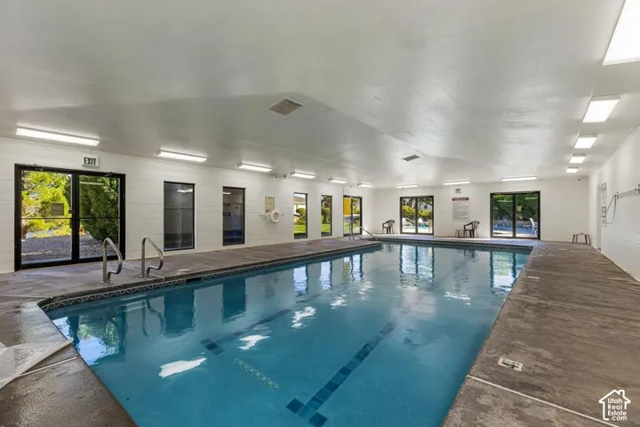 Indoor swimming pool with concrete decking, multiple windows, and exterior access