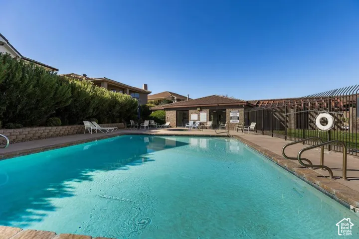 Outdoor swimming pool with concrete decking, surrounding perimeter fencing, and an adjacent brick-clad building