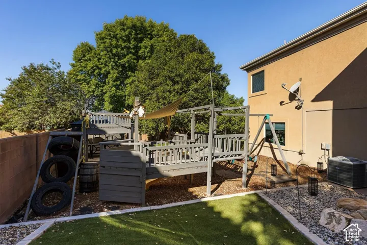 Backyard featuring an artificial turf area, wood-built play structure, a swingset, and a gravel and stone hardscape