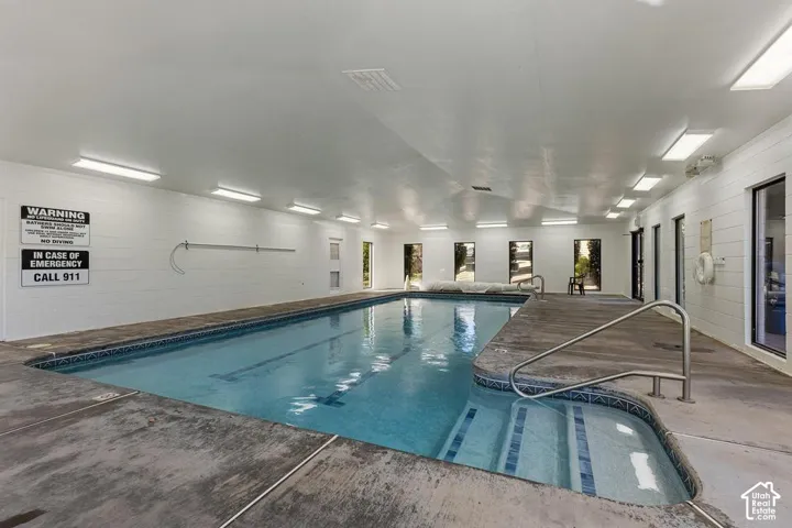 Indoor swimming pool with concrete decking, tiled pool surround, and multiple windows