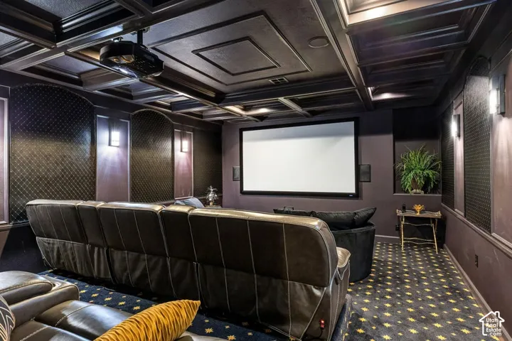 Coffered ceiling with recessed lighting, integrated projector, wall-mounted screen, patterned carpet, and sconce lighting