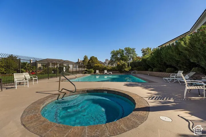 Outdoor pool area featuring a built-in hot tub with stone-finish coping, surrounding concrete decking, and a black wrought iron fence