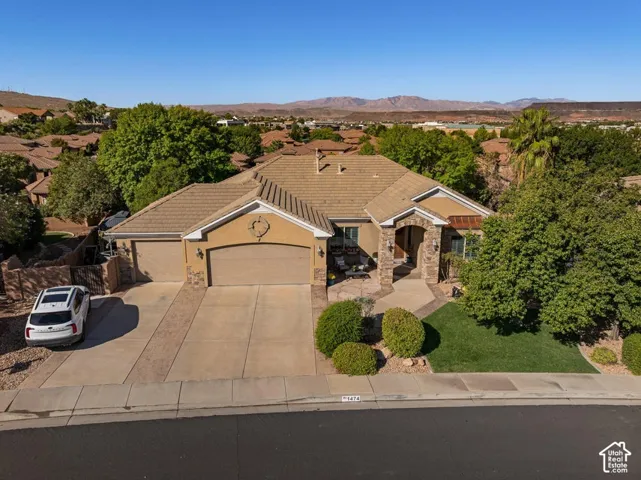 Stucco exterior with stone accents, covered entry, attached multi-car garage, tile roof, and landscaped front yard