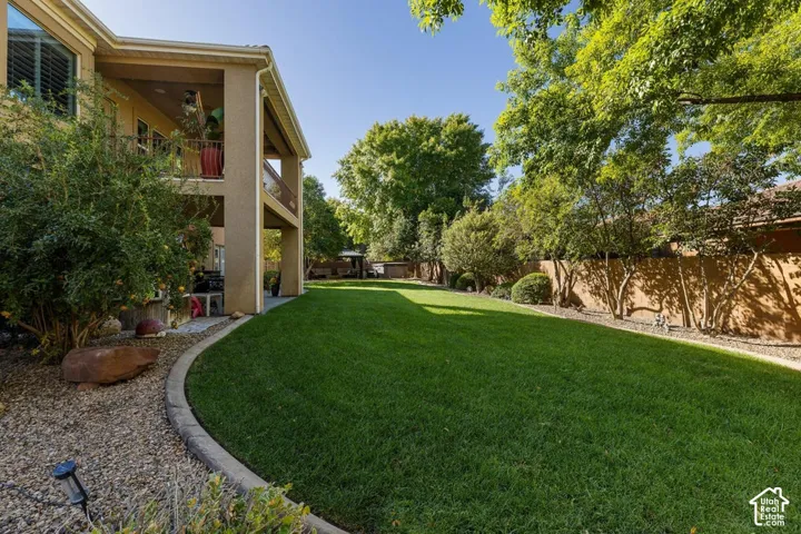 Expansive backyard featuring a manicured lawn, established perimeter landscaping, and a covered patio area
