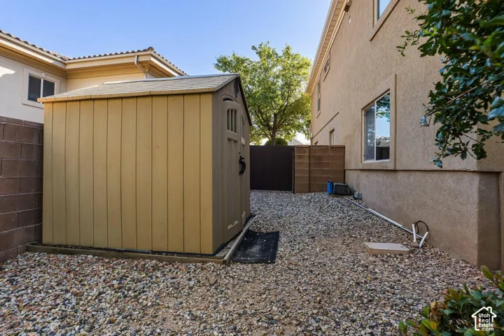 Outdoor storage shed on a gravel-covered property area, featuring a block wall and stucco-sided exterior