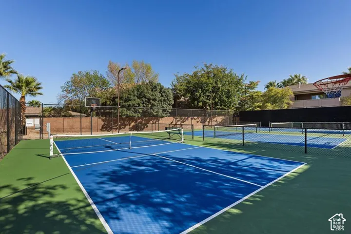 Multiple outdoor courts with blue playing surfaces, green surrounds, and perimeter fencing