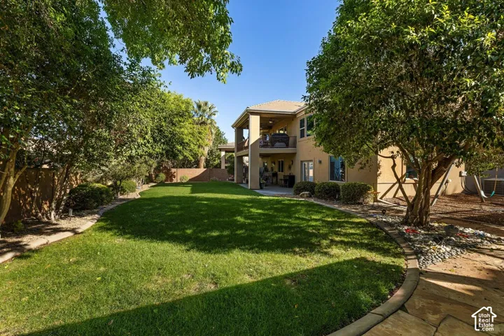 Expansive backyard featuring a manicured lawn, mature trees, and a two-story home with a covered patio and upper-level balcony