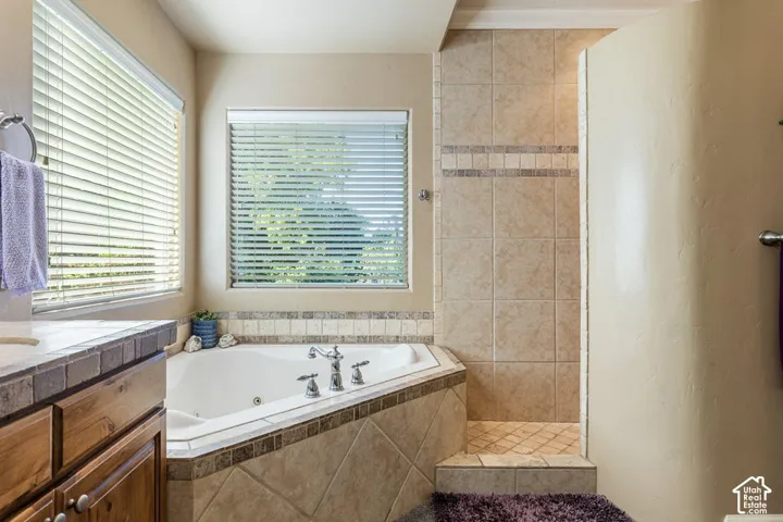 Corner jetted tub with tile surround, walk-in shower with tiled walls and floor, and wood-finish vanity with countertop