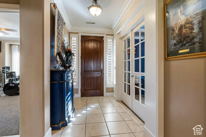 Arched wood-paneled entry door, grid-patterned glass French doors, crown molding, and tile flooring