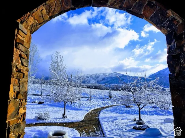 Stone archway framing a mountain backdrop, with a paved walkway and mature trees