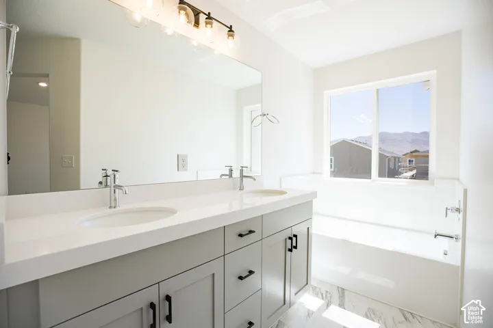 Primary bath with dual sinks, painted wood cabinets, quartz slab countertops, soaker tub and walk-in shower.