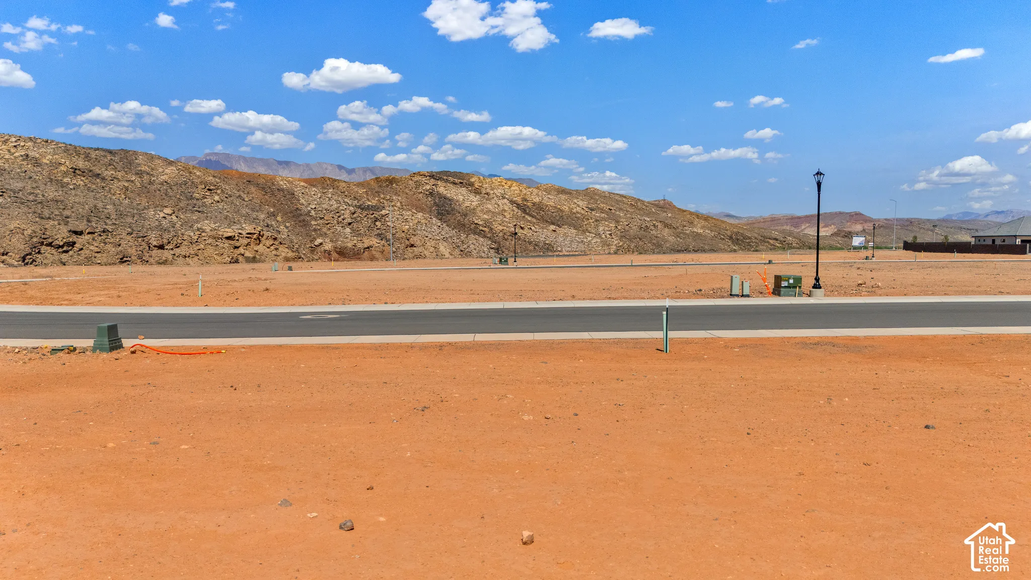 Expansive desert terrain with distant mountainous formations, featuring a paved roadway, street lighting, and utility infrastructure