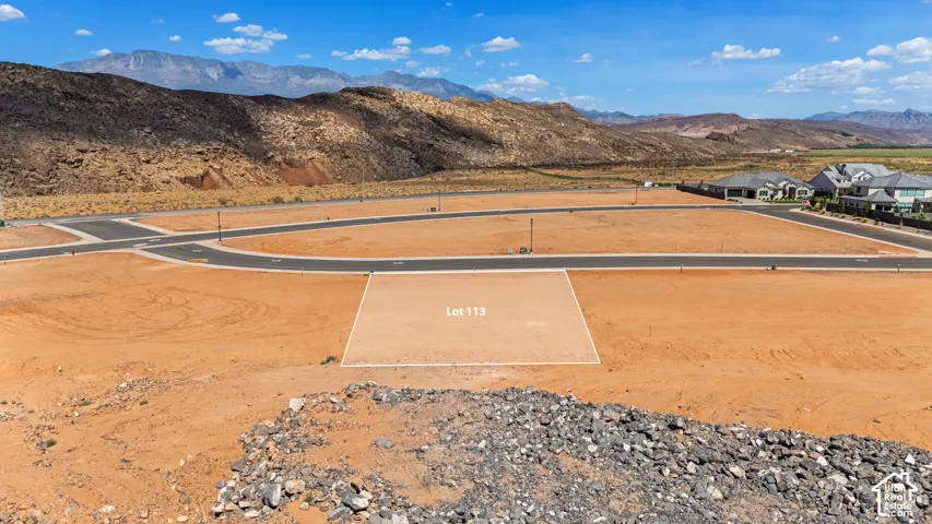 Expansive undeveloped land featuring a level building site, visible Lot 113 marker, and distant mountain backdrop