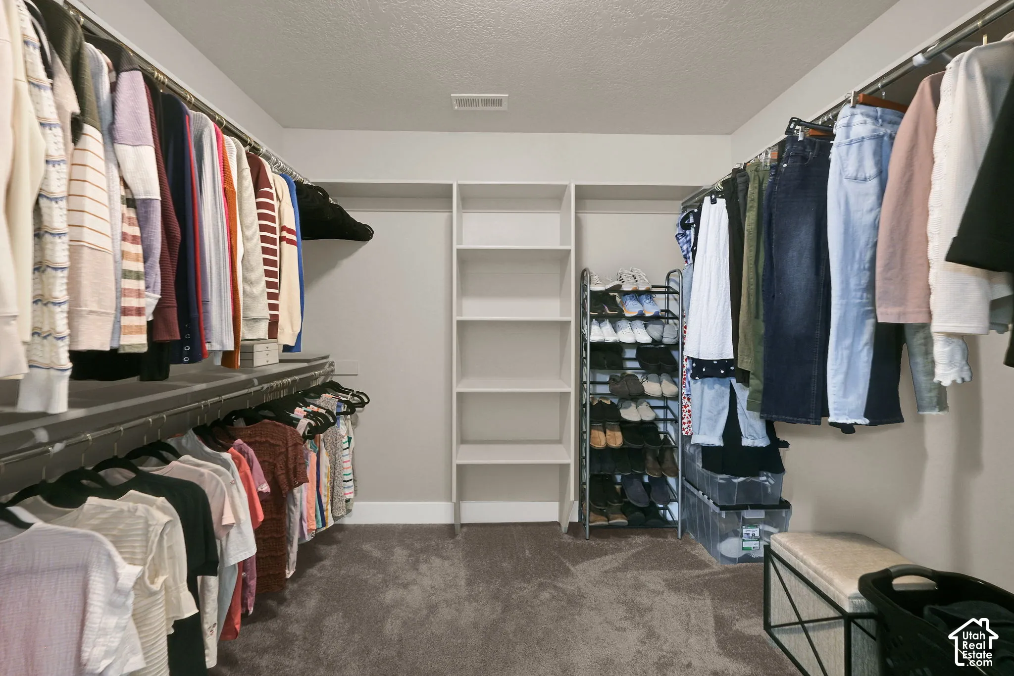 Spacious walk-in closet featuring multiple clothing rods, built-in shelving, and carpet flooring