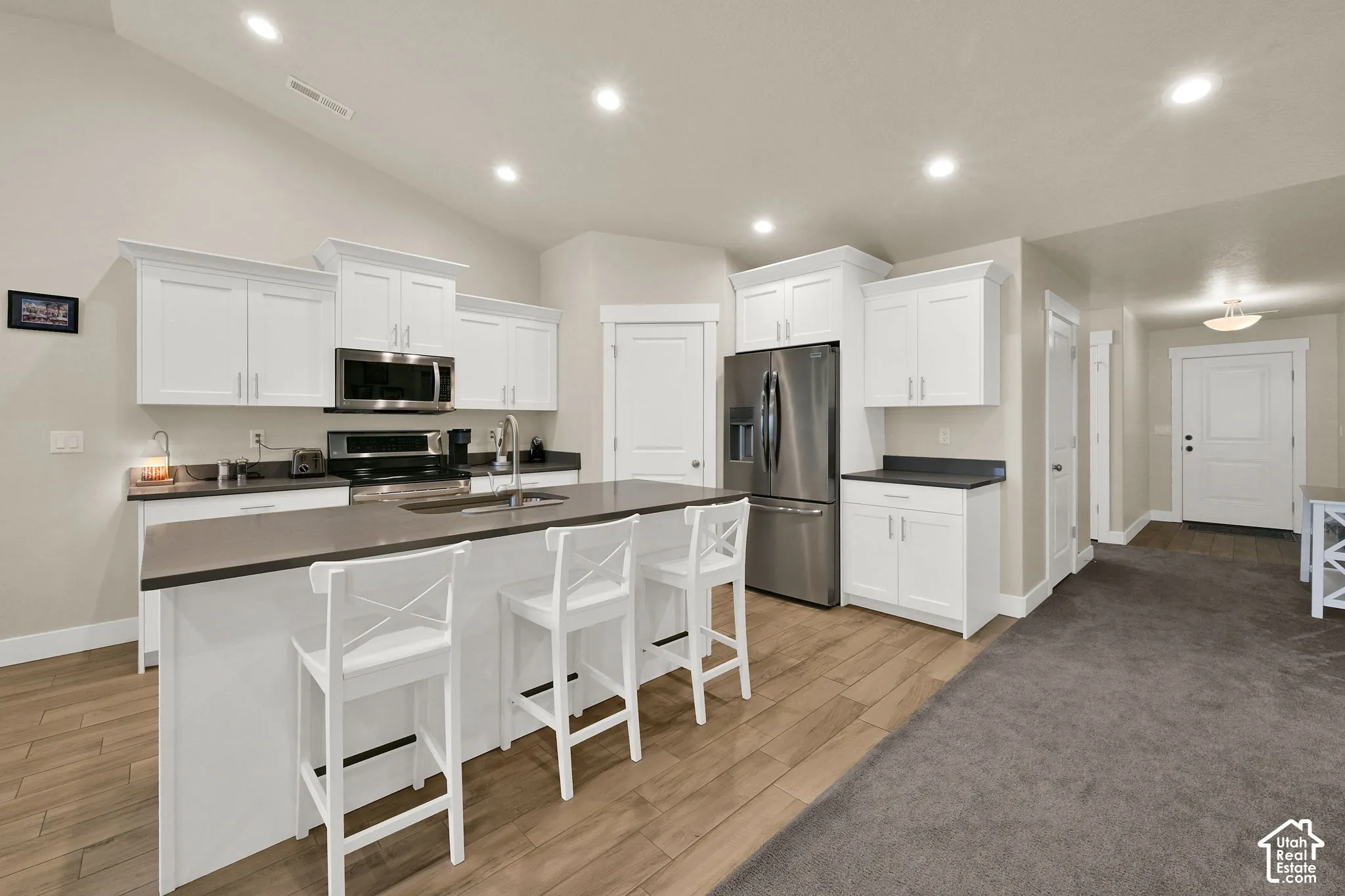 White cabinetry, stainless steel appliances, central island with seating, wood-finish flooring, and recessed lighting