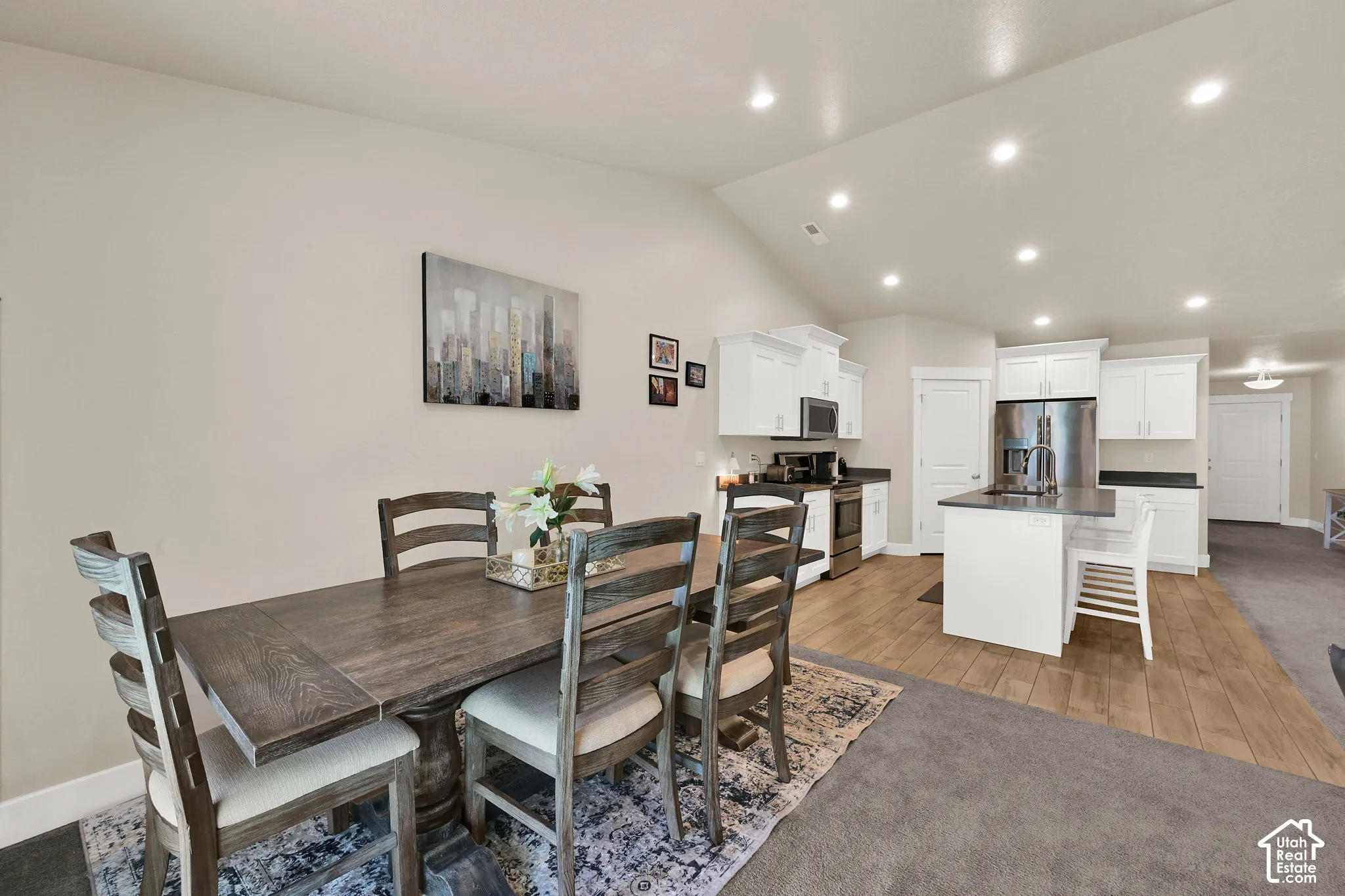 Vaulted ceiling with recessed lighting, white cabinetry, stainless steel appliances, kitchen island with seating, and wood-finish flooring