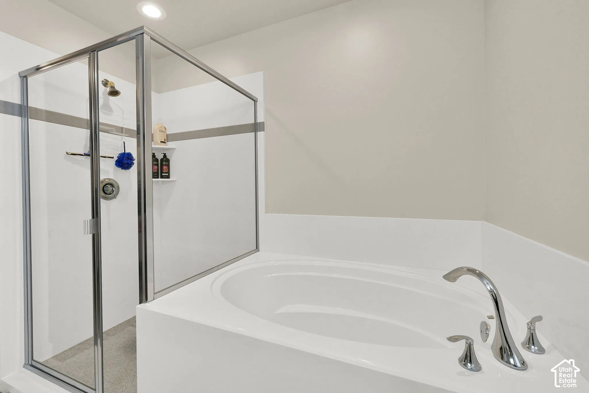 Built-in soaking tub with chrome fixtures, glass-enclosed shower, integrated shower shelving, and recessed lighting