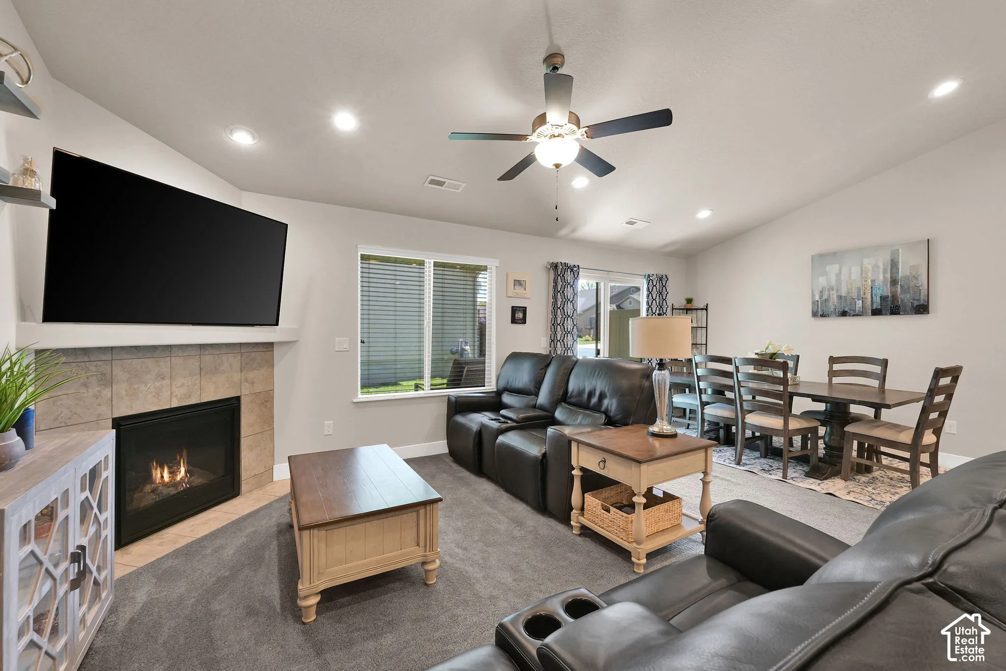 Vaulted ceiling, recessed lighting, ceiling fan, fireplace with tile surround, and sliding glass door