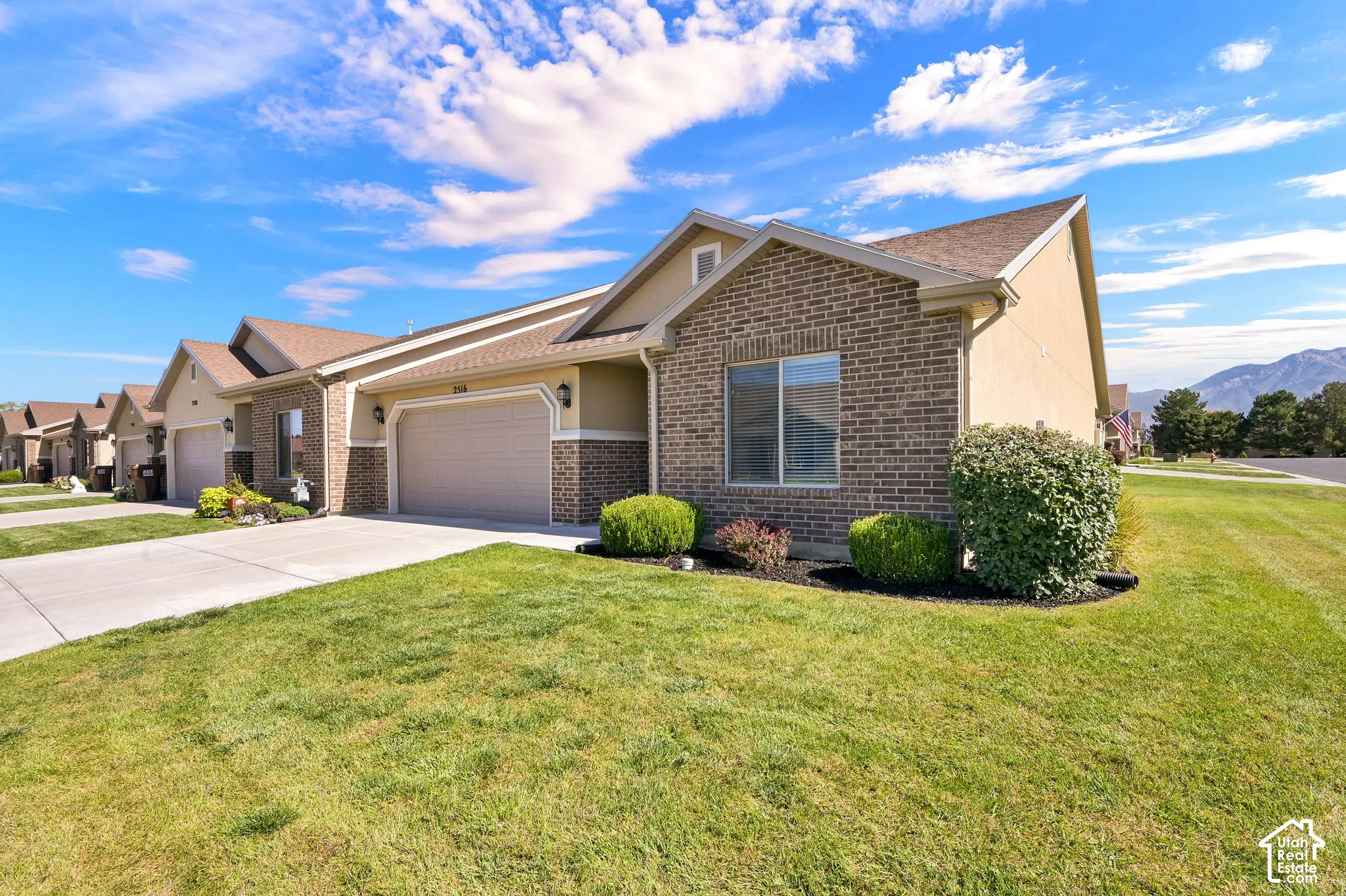 Brick and stucco exterior with an attached garage, paved driveway, and landscaped shrubbery