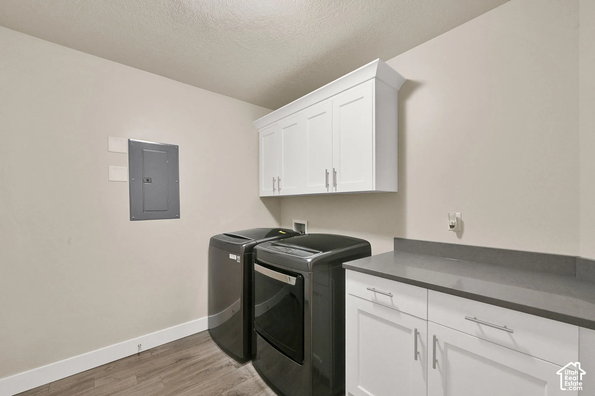 White shaker-style cabinetry with chrome hardware, dark gray countertop, and wood-finish flooring