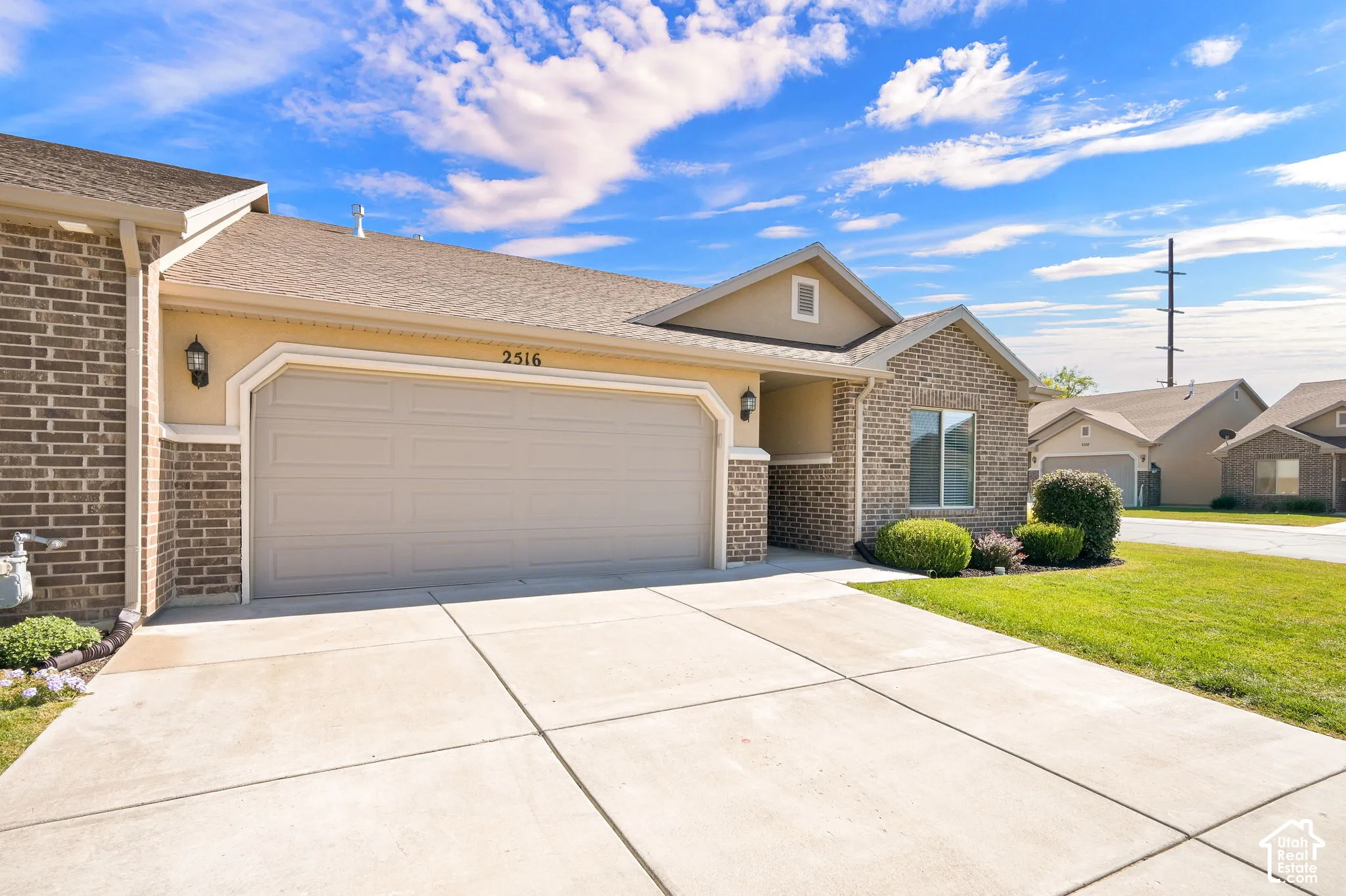 Brick and stucco exterior, attached two-car garage, concrete driveway, and front lawn