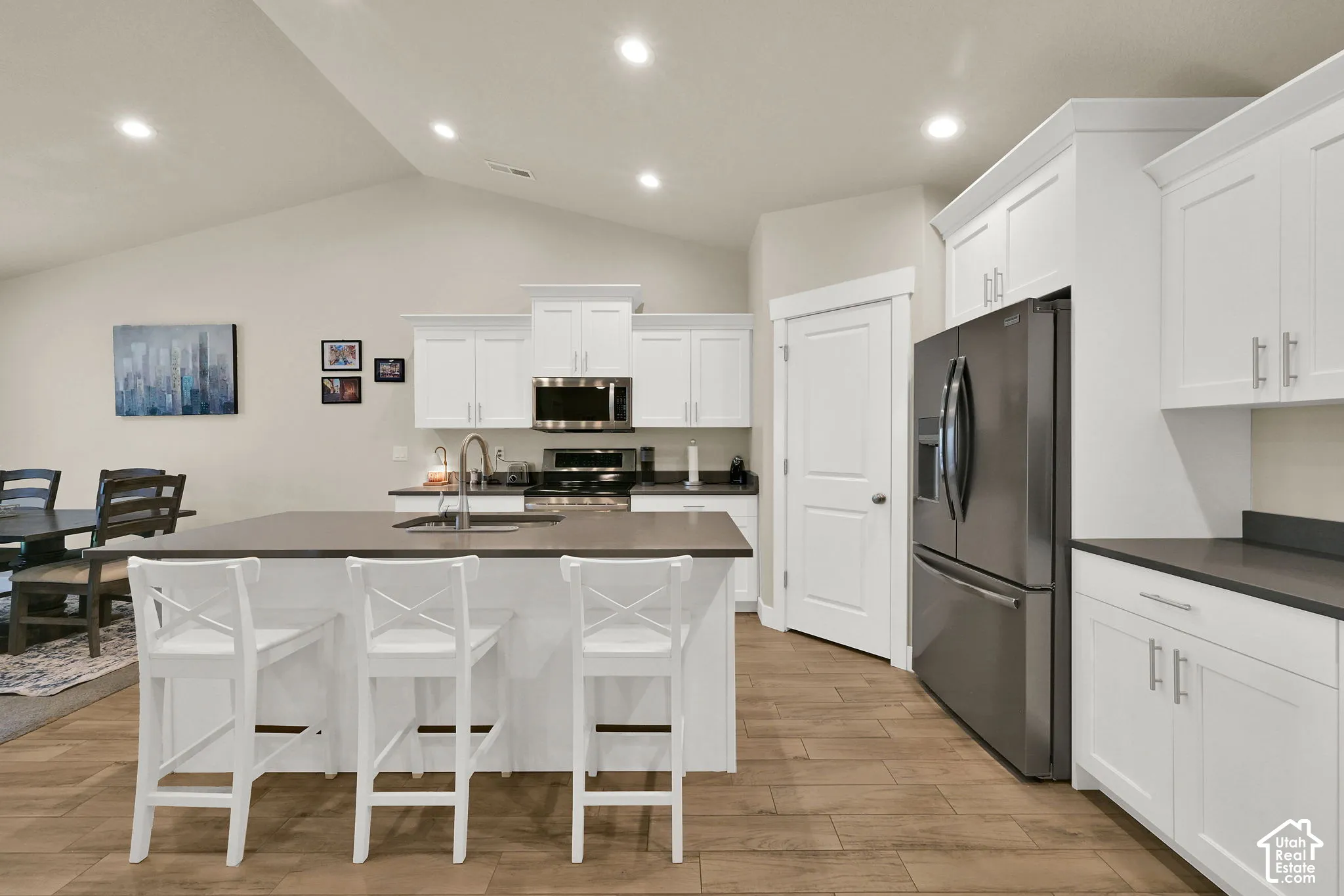 Kitchen featuring wood-finish flooring, white cabinetry, dark countertops, a vaulted ceiling, and stainless steel appliances