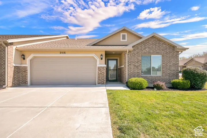 Brick and stucco exterior with an attached garage, concrete driveway, and front lawn